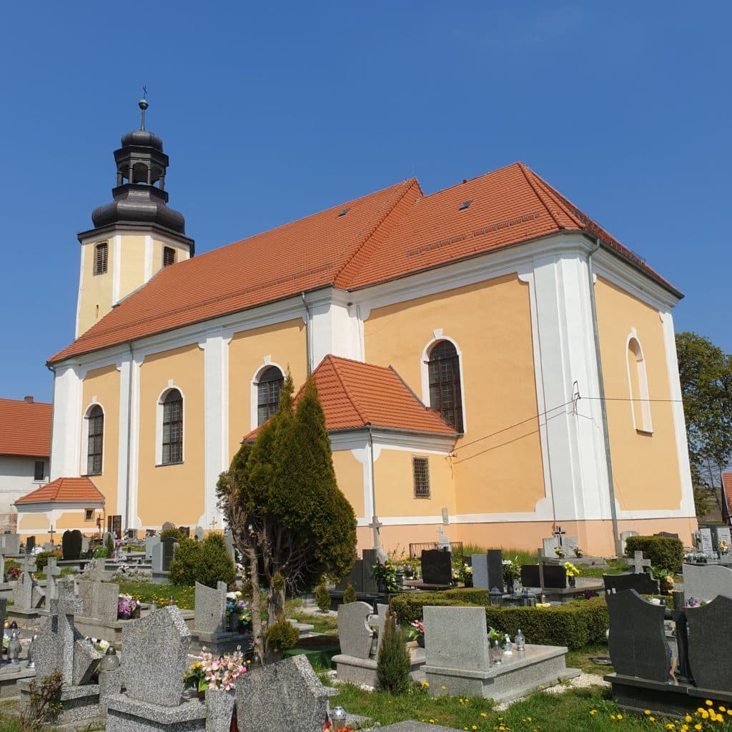 20220501_112504 - Dworek Marmis Kościół z pomarańczową elewacją, czarną wieżą i cmentarz obok, w słoneczny dzień.