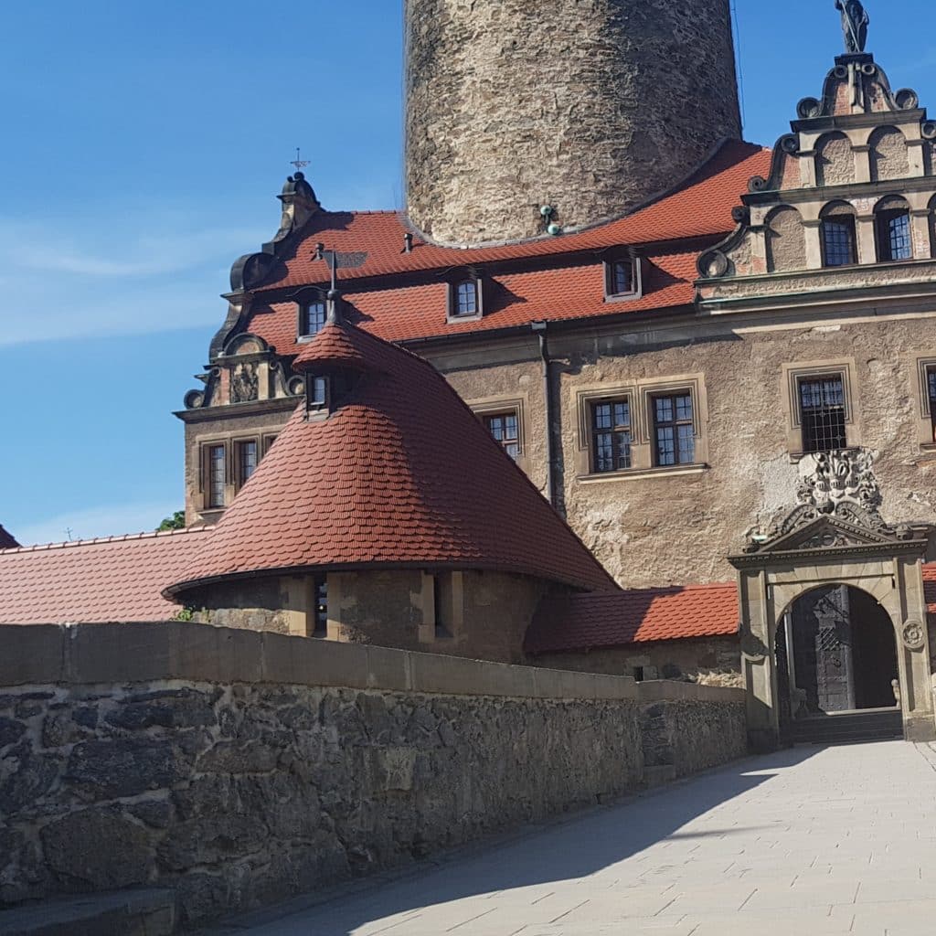 20220505_191738 - Dworek Marmis Zamek z czerwonym dachem, okrągłą wieżą i kamiennym murem, w słoneczny dzień.