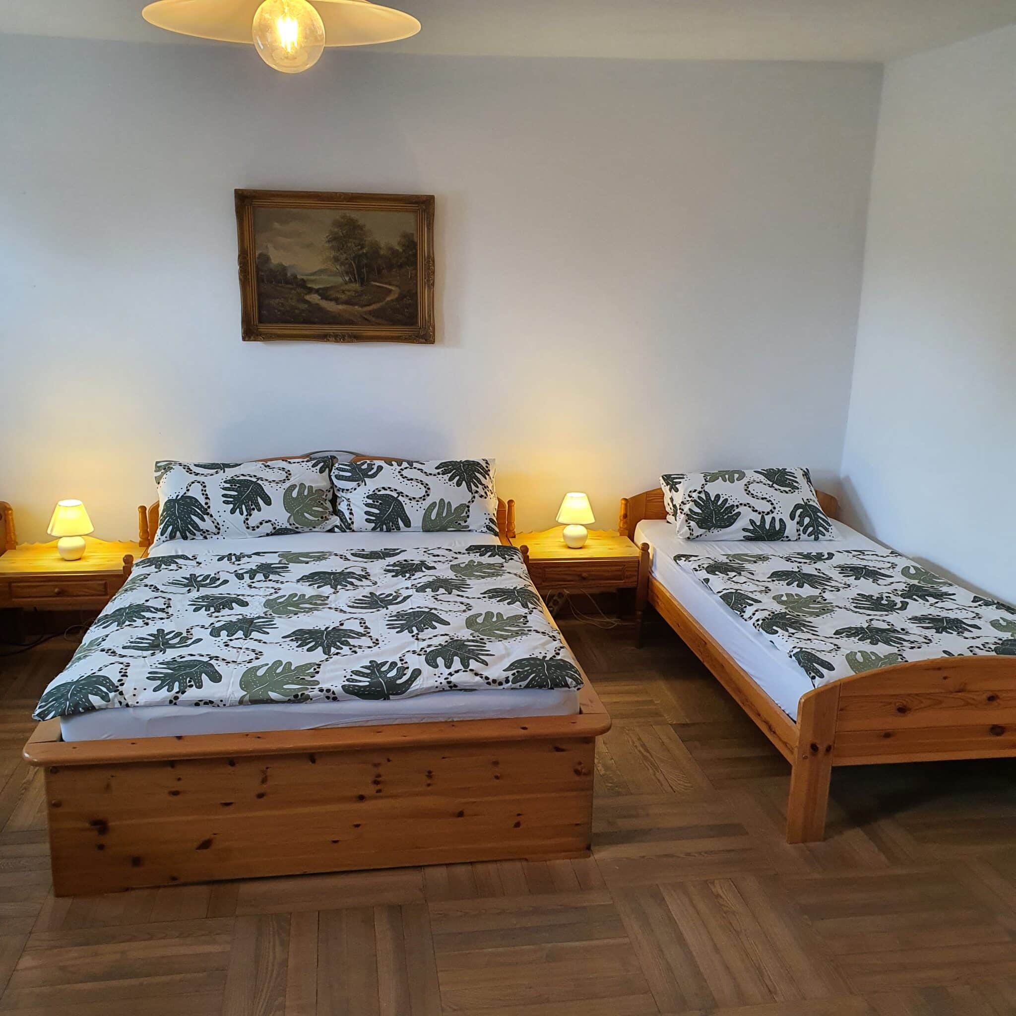 20240727_092417 - Dworek Marmis Dwa łóżka w apartamencie, z pościelą w liście, lampkami nocnymi i obrazem na ścianie.
