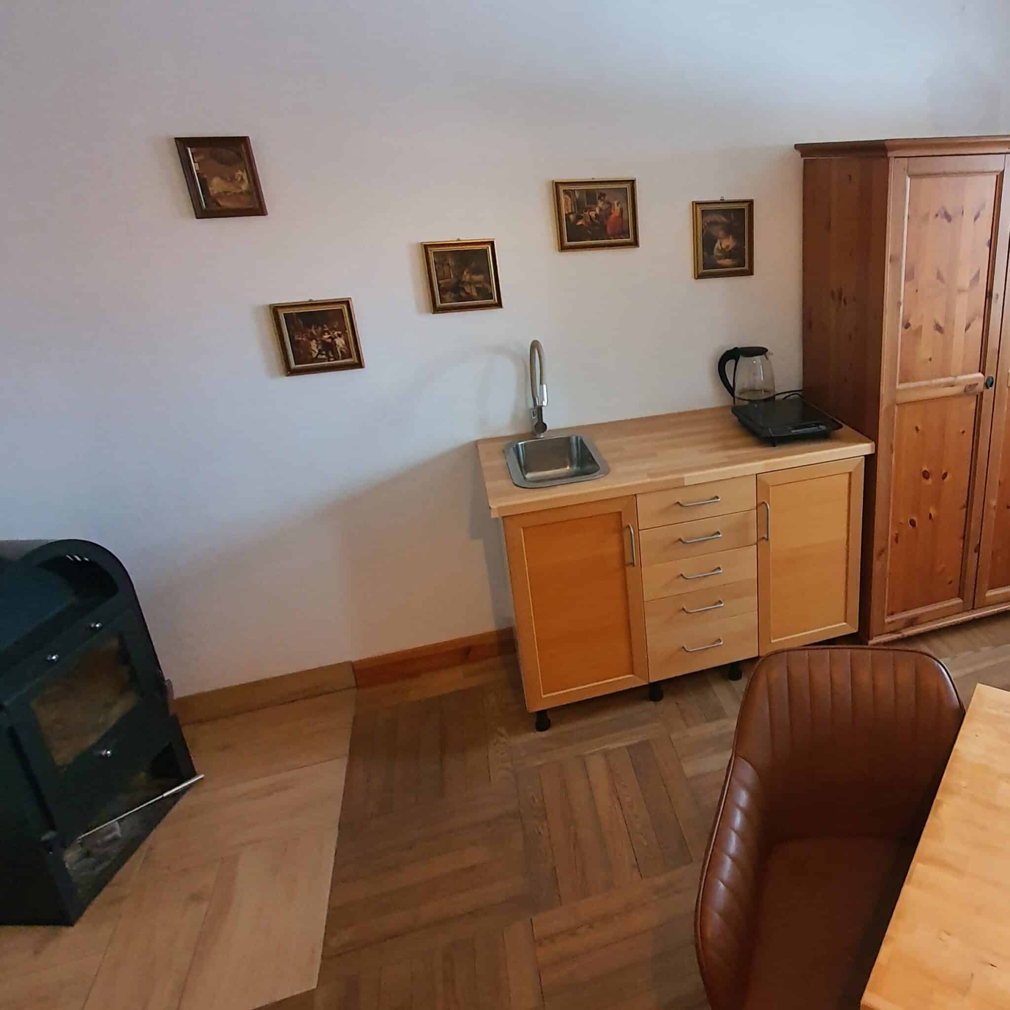 20260130_100047 - Dworek Marmis Kuchnia w apartamencie studio z drewnianymi meblami, zlewem, czajnikiem i obrazami na ścianie.