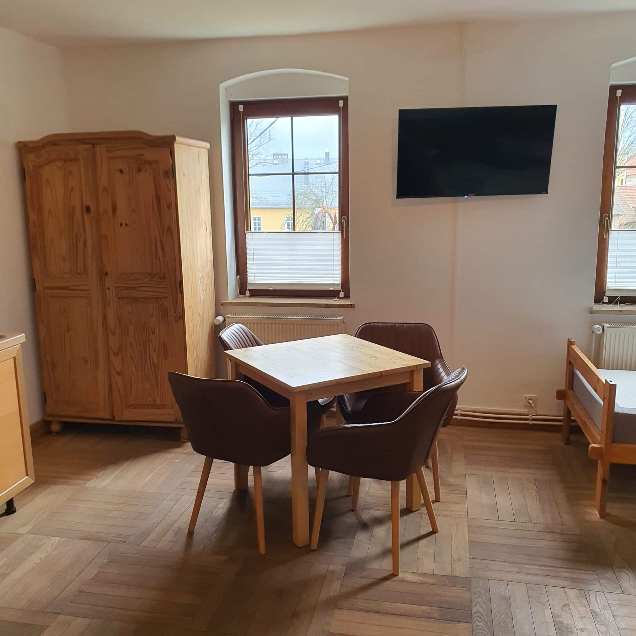 20260326_133803 - Dworek Marmis Stilvolle Wohnungseinrichtung mit Holztisch und Stühlen, TV an der Wand und Kleiderschrank.