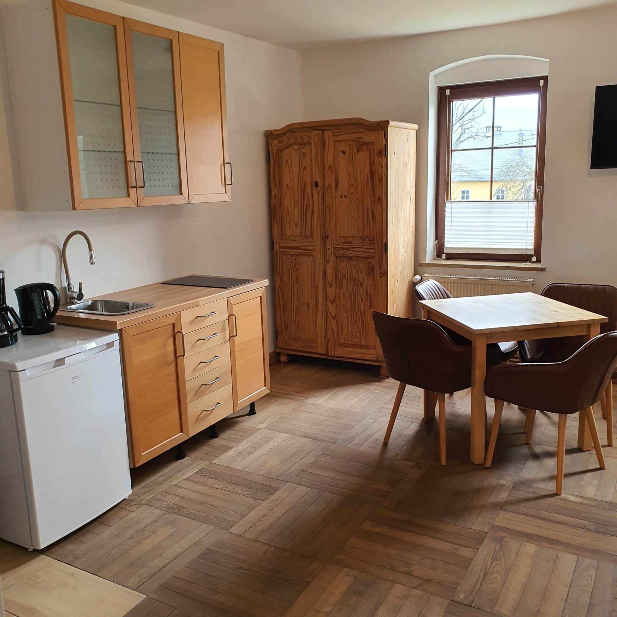 20260326_133817 - Dworek Marmis Moderne Küche in der Studiowohnung mit Holzmöbeln, Tisch und Stühlen.