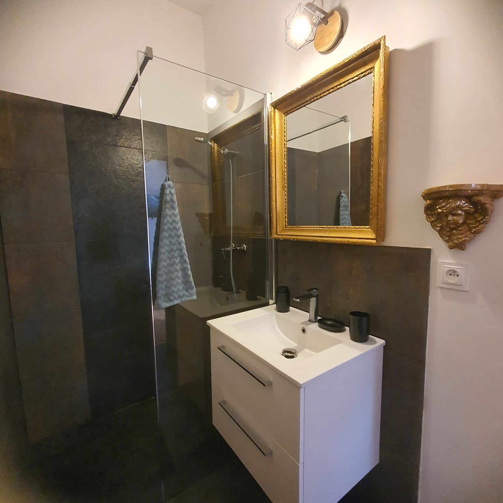 20250924_114853 - Dworek Marmis Nowoczesna łazienka z przeszkloną kabiną prysznicową, złotą ramą lustra i białą szafką umywalkową.