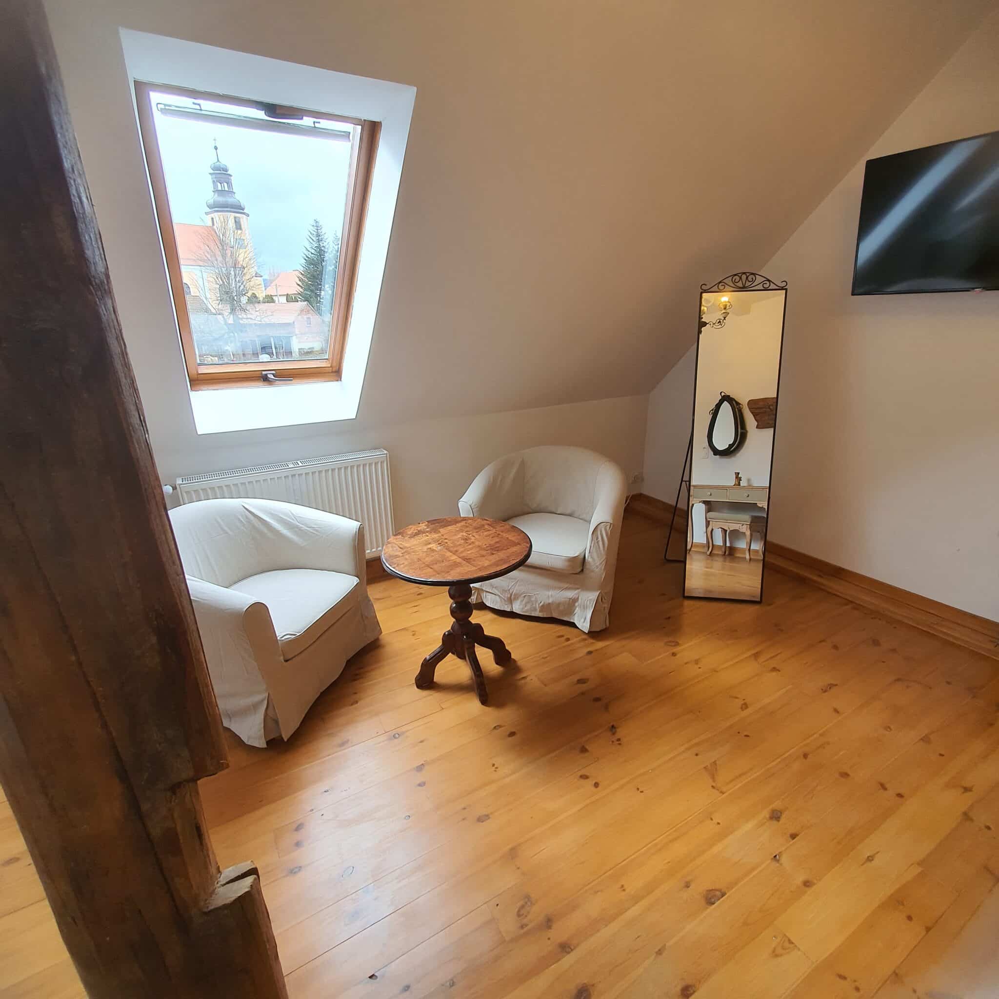 20260212_114011 - Dworek Marmis Dwa białe fotele i okrągły stół w pokoju z drewnianą podłogą, lustrzanym odbiciem i oknem z widokiem.