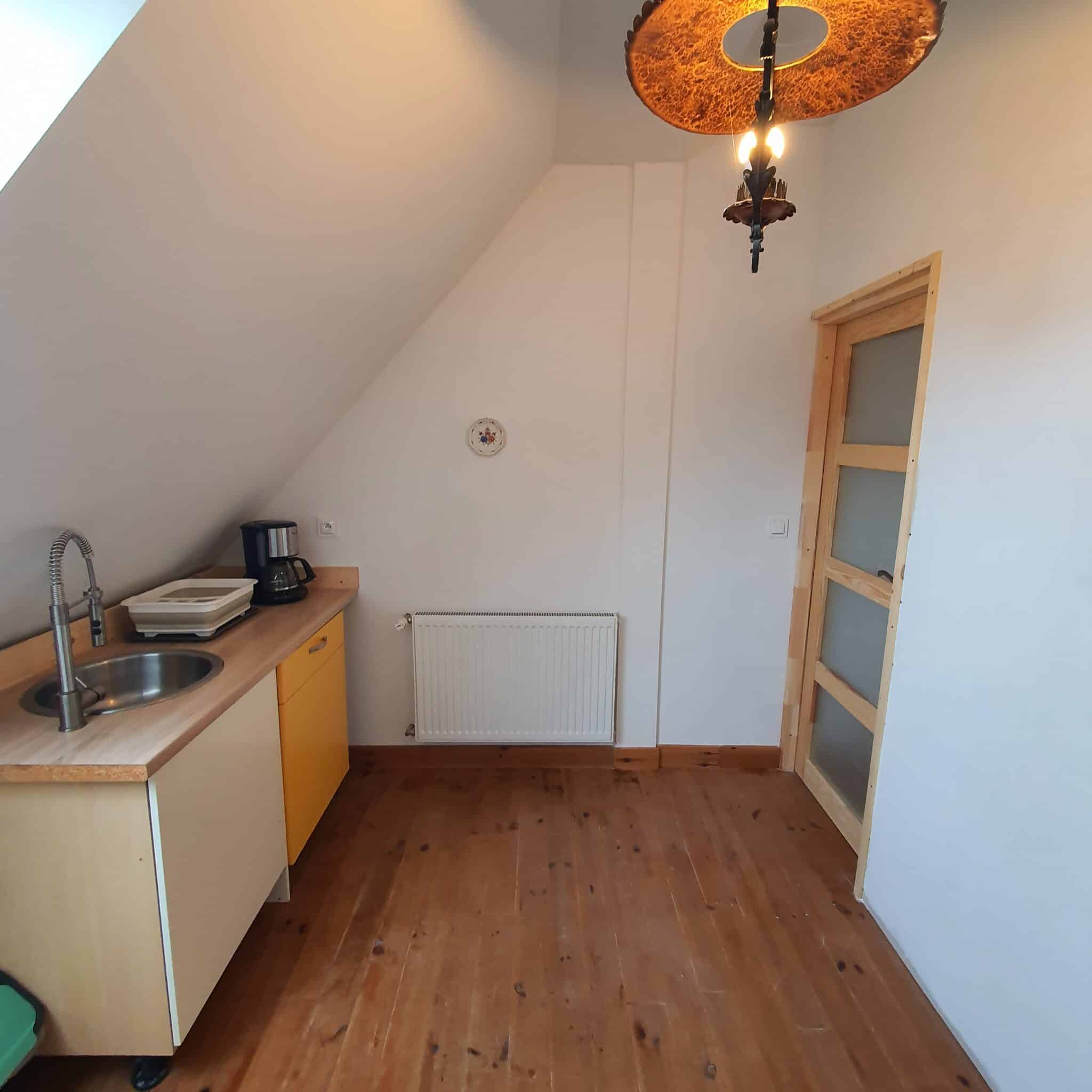 20251206_111639 - Dworek Marmis Gästeküche mit Holzboden, Spüle, Wasserkocher und Schränken in hellen Farben.