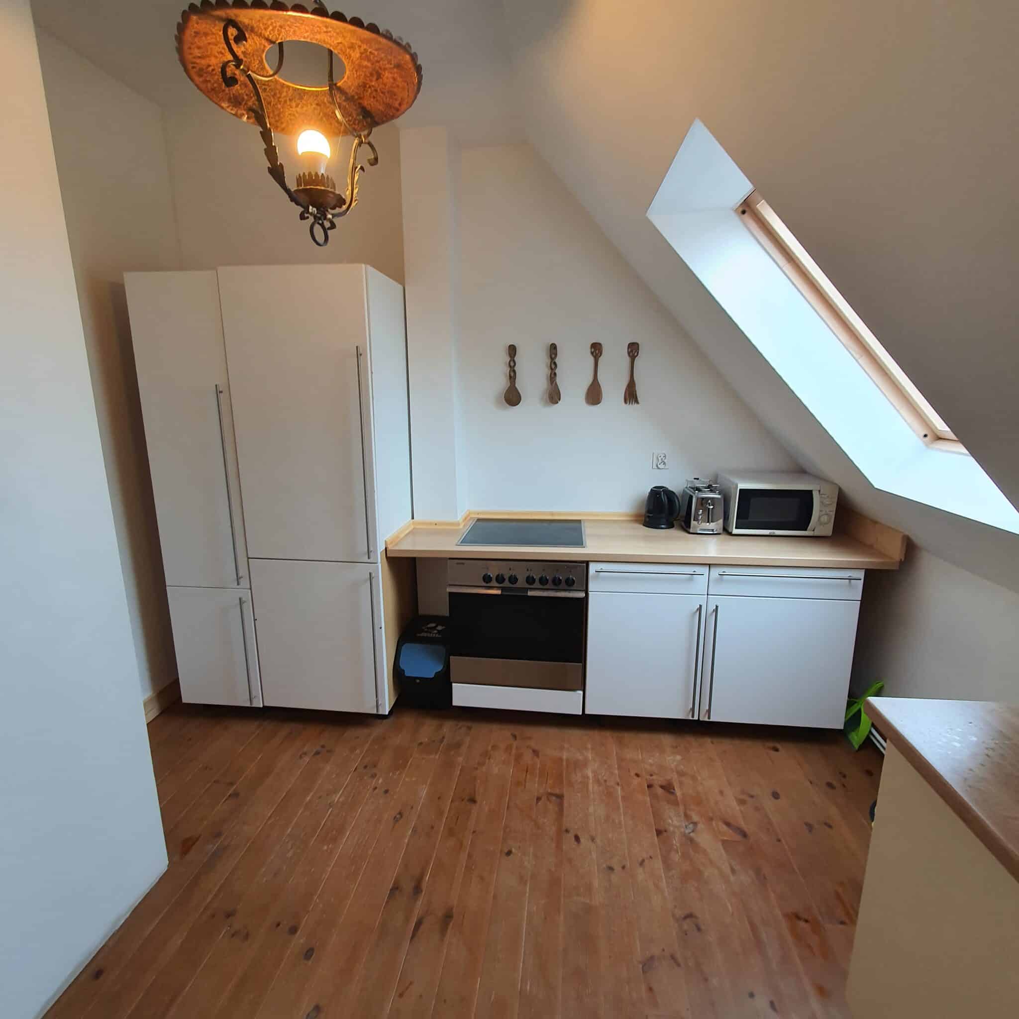 20251206_111700 - Dworek Marmis Gästeküche mit weißen Schränken, Backofen, Mikrowelle und Holzarbeitsplatte. Holzfußboden und Dachfenster.