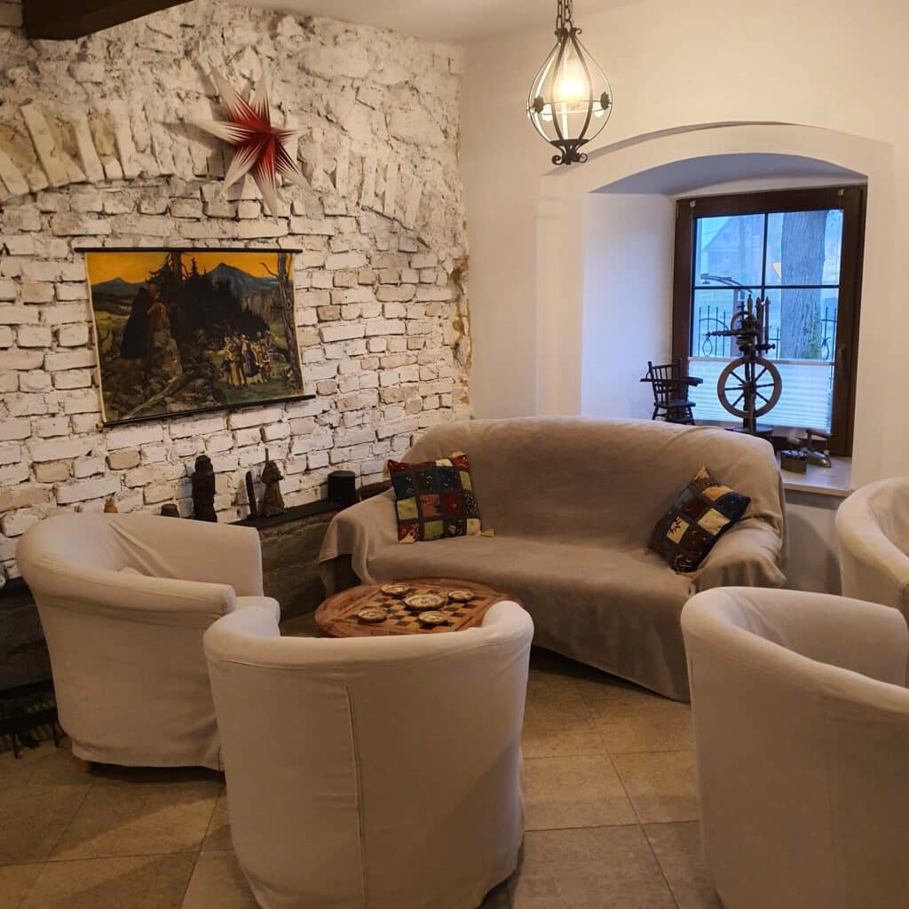 20251223_144617 - Dworek Marmis Przytulny kącik w Dworku Marmis z białą ceglaną ścianą, sofą i fotelami, oraz obrazem na tle.