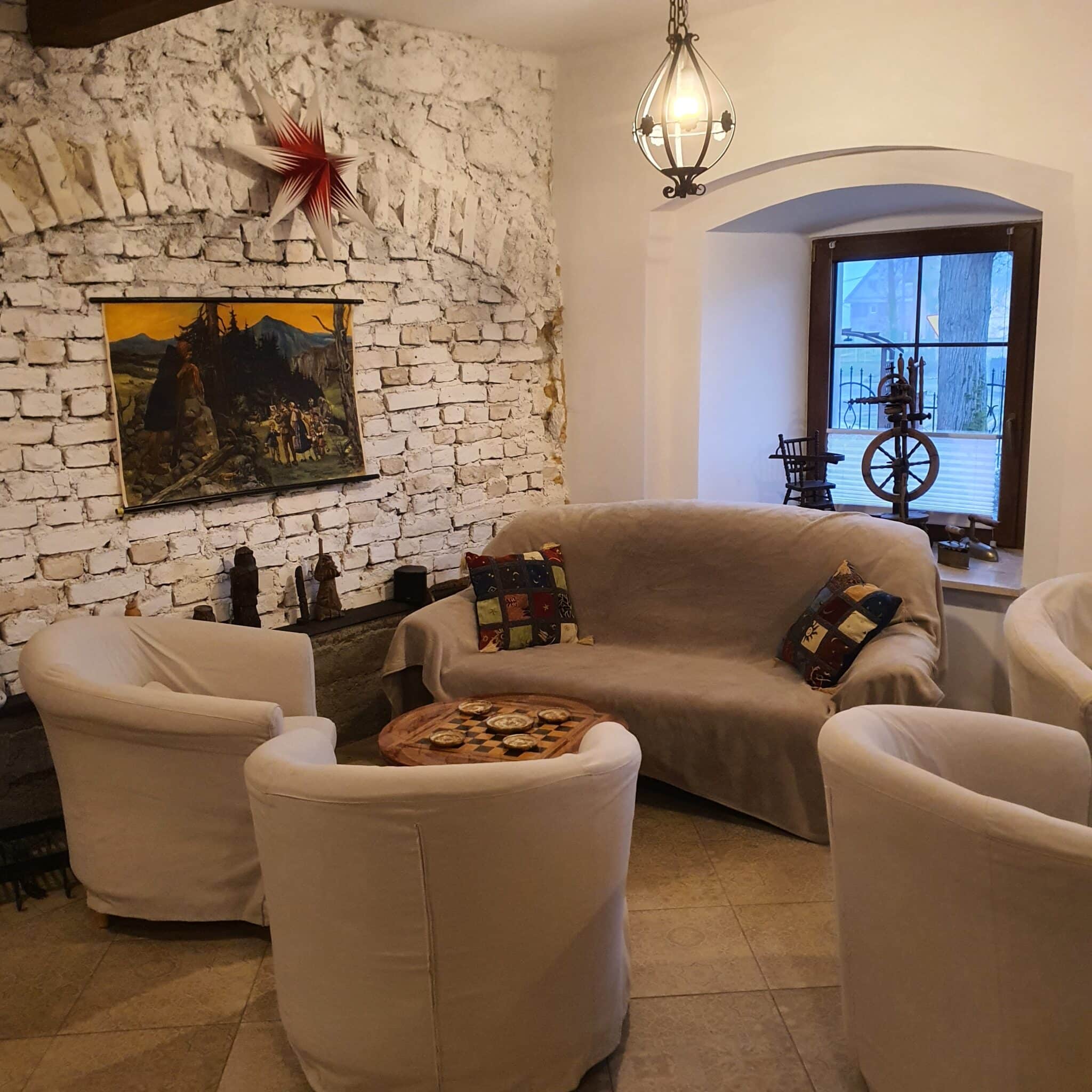 20251223_144617 - Dworek Marmis Przytulny kącik w Dworku Marmis z białą ceglaną ścianą, sofą i fotelami, oraz obrazem na tle.